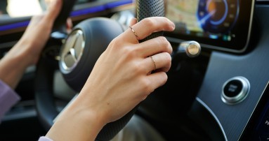 
						  Nahaufnahme einer Hand am Lenkrad eines Mercedes-Benz mit digitalem Cockpit im Hintergrund.
						  