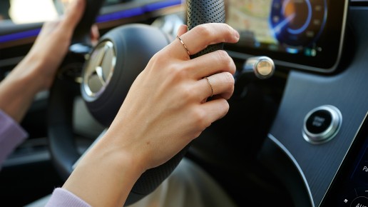 
						  Nahaufnahme einer Hand am Lenkrad eines Mercedes-Benz mit digitalem Cockpit im Hintergrund.
						  