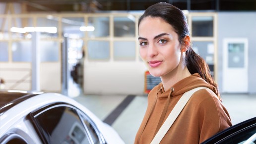 
						  Junge Frau in braunem Hoodie steht l�chelnd neben einem wei�en Mercedes-Benz in einer hellen Werkstattumgebung.
						  