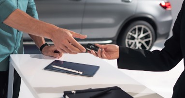 
						  Kunde erh�lt einen Autoschl�ssel von einer Mitarbeiterin �berreicht, im Hintergrund steht ein grauer Mercedes-Benz.
						  