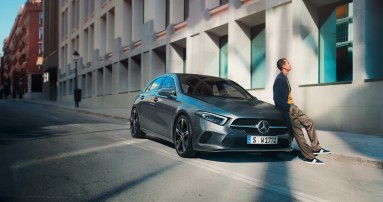 
						  Junger Mann lehnt entspannt an einem geparkten grauen Mercedes-Benz auf einer sonnigen Stadtstra�e vor einem modernen Geb�ude.
						  