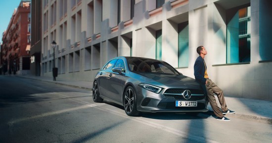 
						  Junger Mann lehnt entspannt an einem geparkten grauen Mercedes-Benz auf einer sonnigen Stadtstra�e vor einem modernen Geb�ude.
						  