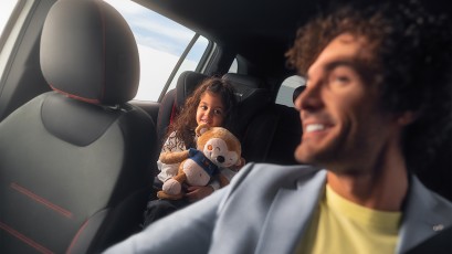 
					  		Mann sitzt l�chelnd im Auto, w�hrend ein Kind im Kindersitz auf der R�ckbank sitzt und ein Kuscheltier h�lt.
					  		