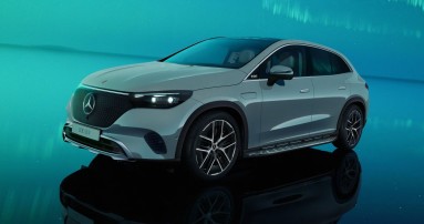
						  Der neue EQE SUV seitlich von vorne in weier Lackierung in einem trkis schimmernden Showroom.
						  