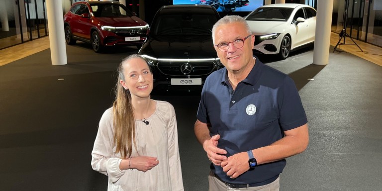 
				Produkttrainerin Joanna Pirpamer und Produkttrainer Michael Thum am Set von „Im Dialog: Mercedes-EQ“ vor drei Mercedes-EQ Modellen.
				