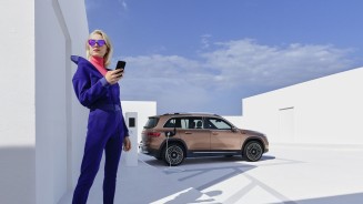 
Eine Frau mit Sonnenbrille hlt ein Smartphone in der Hand, dahinter ldt ein EQA.
