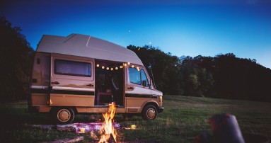 
						  Ein Marco Polo, auf Basis des Mercedes-Benz 209 D, steht mit geffneter Seitentr auf einer Wiese im Abendlicht, vor dem Van brennt ein Lagerfeuer und aus dem Fahrzeuginneren hngt eine Lichterkette heraus.
						  