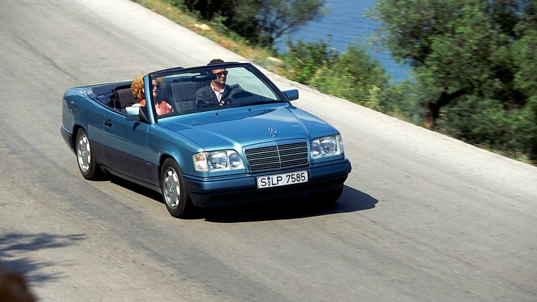 
			Ein Mann und eine Frau fahren in einem Cabriolet der Baureihe 124 auf einer Landstrae.
		