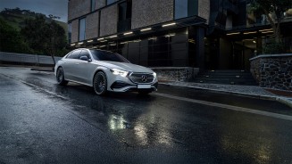 
Eine Mercedes-Benz E-Klasse fhrt mit eingeschalteten Scheinwerfern auf einer verregneten Strae.
