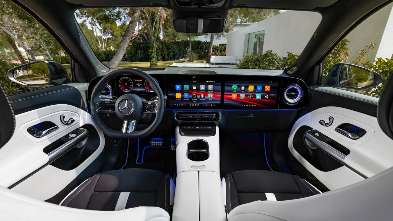 
			Das Bild zeigt das Cockpit des neuen GLB aus der Sicht der R�cksitze. �ber die gesamte Breite des Armaturenbretts verl�uft der Superscreen, bestehend aus drei nebeneinander angeordneten Displays. Darauf sind verschiedene Apps, Fahrzeugfunktionen und Anzeigen zu sehen. Die Innenausstattung ist zweifarbig in Schwarz und Wei� gehalten, erg�nzt durch blaue Lichtakzente in der Mittelkonsole und im Fu�raum.
		