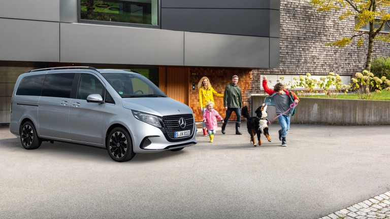 
			Eine Mercedes-Benz V-Klasse in hightechsilber metallic parkt in der Einfahrt vor einem Familienhaus, daneben luft eine vierkpfige Familie mit ihrem Hund.
		
