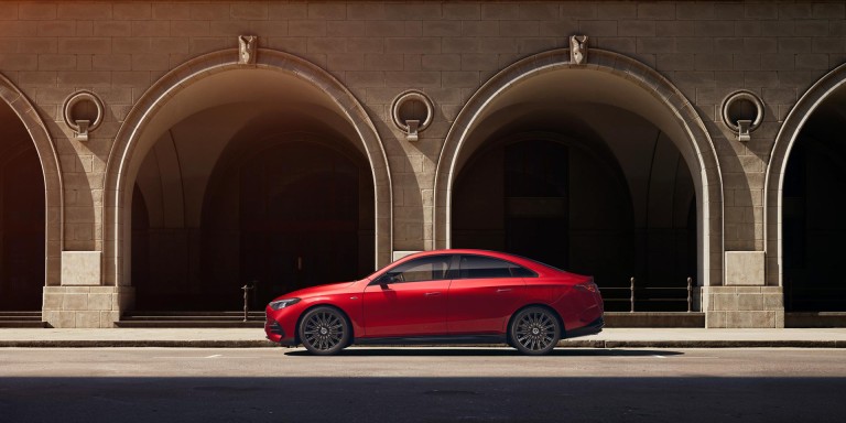 
				Der neue Mercedes-Benz CLA mit EQ Technologie in Patagonienrot fhrt vor Arkaden auf einer Strae. 
				