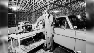 
Schwarz-Wei-Aufnahme eines Mercedes-Benz Ingenieurs, der mit Kopfhrern in einem schallisolierten Raum neben einem alten Mercedes-Benz Fahrzeug steht und Akustiktests durchfhrt.
