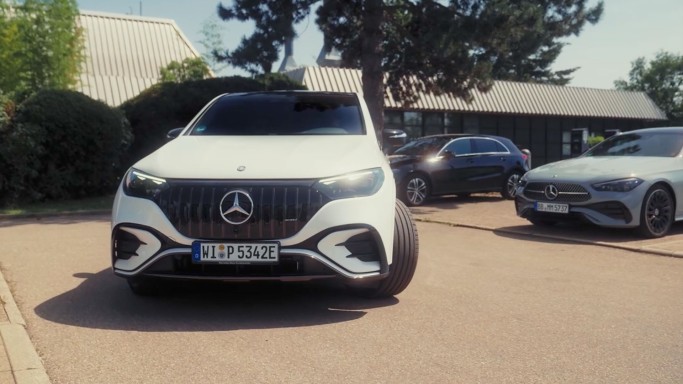 
				Frontalansicht eines wei�en EQE SUV mit eingeschlagenen Vorderr�dern, der gerade r�ckw�rts auf einem Parkplatz eingeparkt wird. Im Hintergrund stehen zwei weitere Mercedes-Benz Fahrzeuge.
				