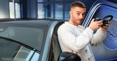 
						  Produktmanager Christopher Hartung lehnt an einer Mercedes-Benz E-Klasse. Er trgt eine weie Jacke und hlt Kopfhrer in der Hand. Im Hintergrund rechts ist eine vergrerte Aufnahme eines Burmester Lautsprechers zu sehen.
						  