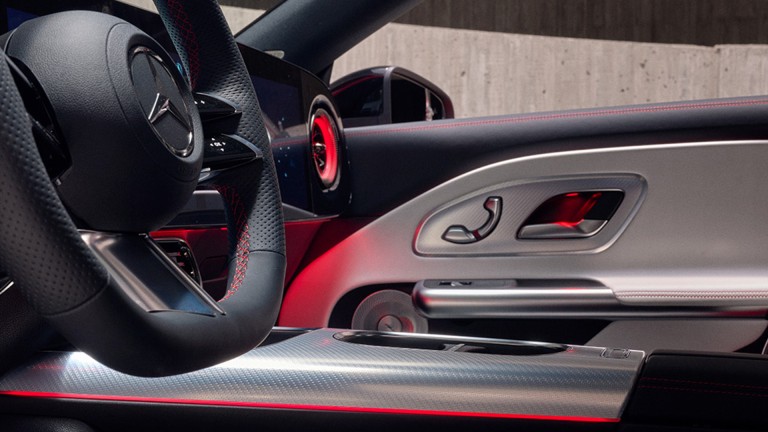 
			Nahaufnahme des Cockpits eines Mercedes-Benz CLA mit AMG-spezifischem Multifunktionslenkrad, Zierelementen in Aluminium mit Carbonschliff hell und roter Ambientebeleuchtung.
		