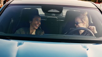 
Blick durch die Windschutzscheibe eines Mercedes-Benz Fahrzeugs auf die vorderen Sitze: Links sitzt eine dunkelhaarige Frau auf dem Beifahrersitz, rechts eine blonde Frau mit Sonnenbrille auf dem Fahrersitz. Beide lachen sich an.

