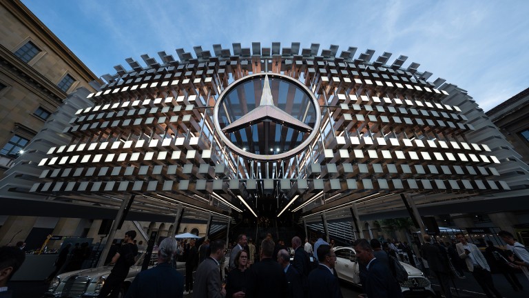 
			Beleuchtete Skulptur eines �berdimensionalen Mercedes-Benz K�hlergrills mit Stern im Apothekenhof der Residenz. Im unteren Bildbereich gehen G�ste unter der Installation hindurch.
		