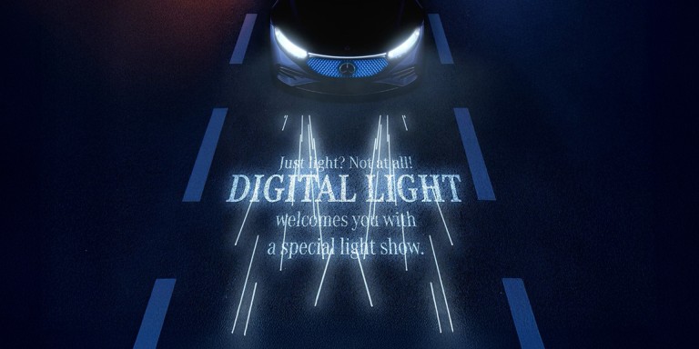 
				Die Scheinwerfer eines Mercedes-Benz projizieren mit DIGITAL LIGHT einen Schriftzug auf die Strae: „Just light? Not at all! DIGITAL LIGHT welcomes you with a special light show.“
				