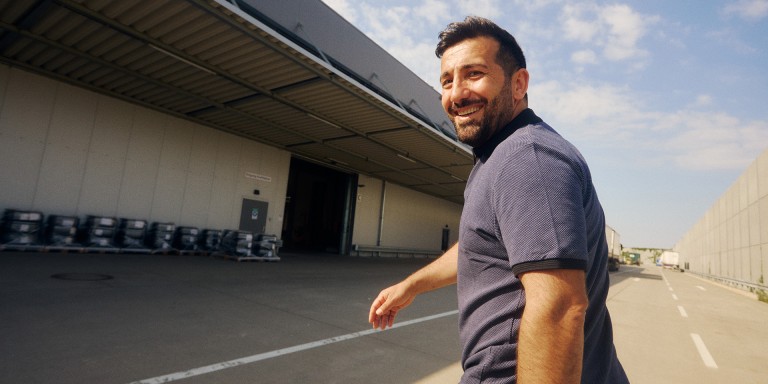 
				Ali Tas, Produktmanager Sonderausstattung „Winterkomplettrder ab Werk 8-fach Bereifung“ bei Mercedes-Benz Customer Solutions GmbH, luft drauen vor dem Rderlager in Zwickau und blickt lchelnd in die Kamera.
				