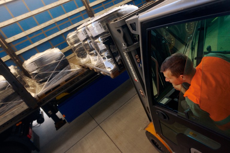 
			Ein Gabelstaplerfahrer in Warnweste ldt verpackte Reifenpaletten auf einen LKW.
		