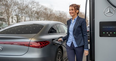 
						  Eine Frau in dunkelblauer Office-Kleidung ldt ihren vollelektrischen Mercedes-Benz an der Ladesule eines Mercedes-Benz Charging Hubs auf.
						  