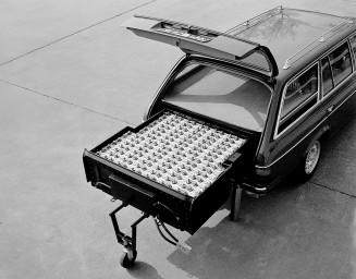 
Schwarz-Wei�-Aufnahme des ge�ffneten Kofferraums eines Mercedes-Benz T-Modells der Baureihe 123. Im Kofferraum ist die gro�e Nickel-Eisen-Batterie sichtbar, die fast den gesamten Platz einnimmt und herausgezogen auf einem St�tzrad steht.
