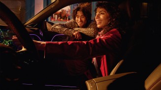 
Eine Frau sitzt auf dem Beifahrersitz eines Mercedes-Benz Fahrzeugs und bedient lchelnd das Zentraldisplay. Neben ihr beugt sich ein Mann zum Beifahrerfenster herein und sttzt sich lchelnd auf der Fensterffnung ab.
