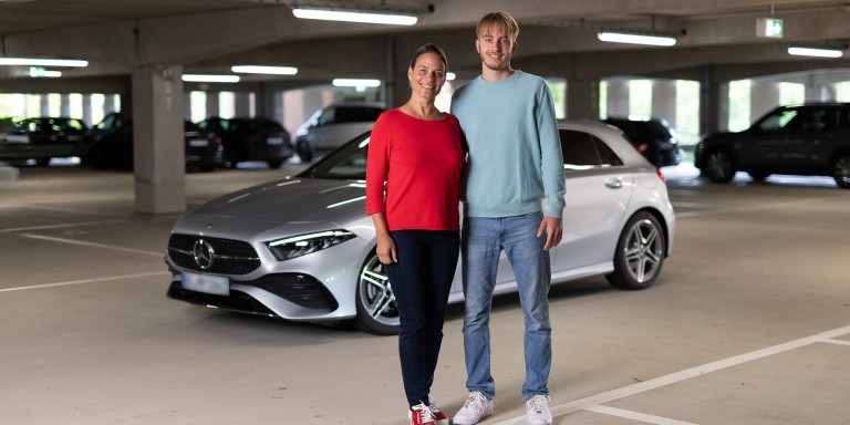 
				Susanne Gutmann (links) und ihr Sohn Leon stehen in einem Parkhaus vor einer silbernen A-Klasse. Im Hintergrund sind weitere Fahrzeuge zu sehen.
				