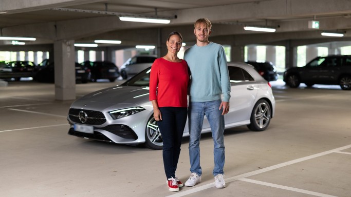 
				Susanne Gutmann (links) und ihr Sohn Leon stehen in einem Parkhaus vor einer silbernen A-Klasse. Im Hintergrund sind weitere Fahrzeuge zu sehen.
				