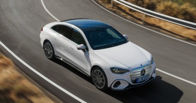 
					  Die neue elektrische Mercedes-Benz C-Klasse in MANUFAKTUR opalithwei� metallic bright f�hrt durch eine lang gezogene Linkskurve auf einer Landstra�e. Sichtbar sind die flie�ende coup�hafte Silhouette und das schwarze Panoramadach. Links und rechts der Fahrbahn ist eine trockene, h�gelige Landschaft zu sehen.
					  