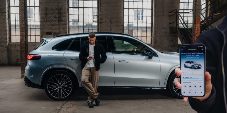 
				Christopher Hartung von Mercedes-Benz lehnt an einem silbernen Mercedes-Benz Fahrzeug und schaut auf sein Handy in seiner rechten Hand, am rechten Bildschirmrand ist ein Handy eingeblendet, auf dem die Mercedes-Benz App ge�ffnet ist.
				
