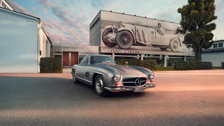 
			Ein silberner Mercedes-Benz 300 SL aus den 1950er-Jahren steht vor dem Mercedes-Benz Classic Center. Das Fahrzeug ist von schr�g vorne zu sehen, mit markanter Front, gro�em Mercedes-Stern im K�hlergrill und geschlossener Karosserie.
		