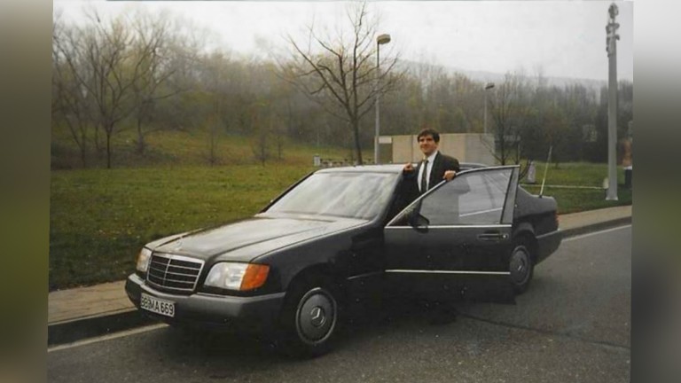 
			Ein Bild aus den 1990ern zeigt den ehemaligen Mercedes-Benz Members Mitarbeiter Eckhard Dunkel, wie er neben der ge�ffneten Fahrert�r einer S-Klasse der Baureihe 140 steht, die neben einer Wiese geparkt ist.
		