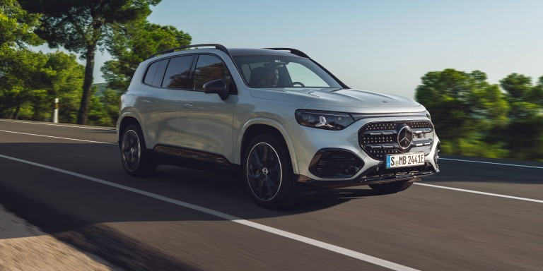 
				Vorderansicht des elektrischen Mercedes-Benz GLB in Hightechsilber, der auf einer Landstra�e f�hrt. Entlang der Stra�e sind gr�ne B�ume und Vegetation zu sehen, dar�ber ein klarer Himmel.
				