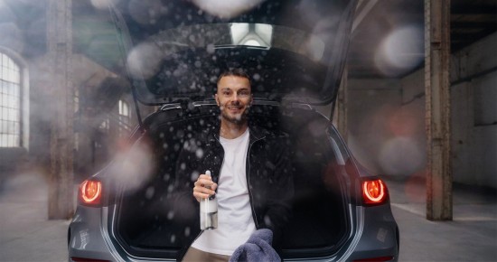 
					  Frontaler Blick auf den ge�ffneten Kofferraum eines Mercedes-Benz GLC, in dem Christopher Hartung sitzt, in der linken Hand einen Putzlappen und in der rechten Hand eine Putzmittelspr�hflasche h�lt, mit der er in die Kamera spr�ht. Bekleidet ist Christoph mit einem wei�en T-Shirt und einer schwarzen Jacke mit Rei�verschluss.
					  