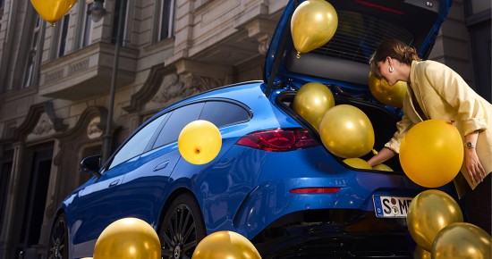 
					  Eine Frau in einem gelben Blazer beugt sich in den ge�ffneten Kofferraum eines Mercedes-Benz CLA Shooting Brake in der Farbe klarblau metallic, aus dem goldene und gelbe Luftballons herausstr�men. Einige Ballons schweben bereits um das Fahrzeug herum, andere befinden sich noch im Kofferraum.
					  