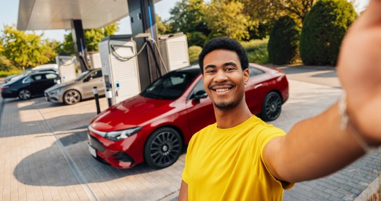 
					  Ein Mann in gelbem T-Shirt steht l�chelnd vor einem elektrischen CLA in MANUFAKTUR patagonienrot metallic, der an der Lades�ule eines Ladeparks steht, und mit der linken Hand ein Selfie aufnimmt.
					  