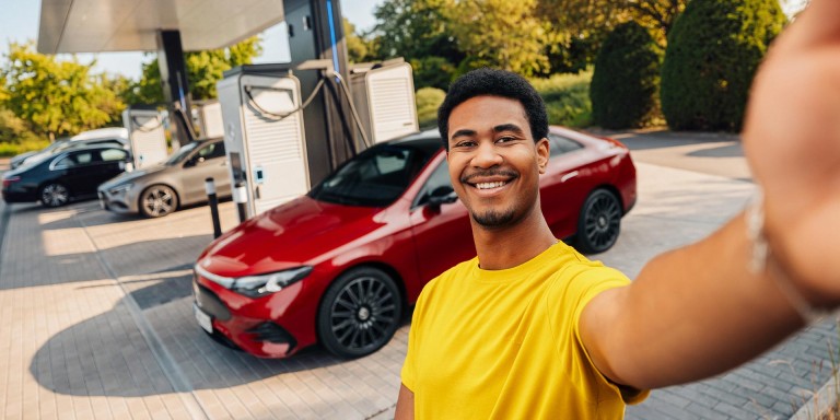 
				Ein Mann in gelbem T-Shirt steht l�chelnd vor einem elektrischen CLA in MANUFAKTUR patagonienrot metallic, der an der Lades�ule eines Ladeparks steht, und mit der linken Hand ein Selfie aufnimmt.
				