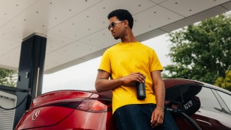 
Ein junger Mann tr�gt Sonnenbrille, ein gelbes T-Shirt und eine dunkelblaue Jeans. Er lehnt am Heck eines elektrischen CLA in MANUFAKTUR patagonienrot metallic, der an einer Lades�ule geladen wird. In der Hand h�lt er einen schwarzen Kaffeebecher mit Mercedes-Benz Branding.
