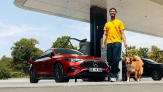 
Ein Mann im gelbem T-Shirt und dunkler Jeans f�hrt einen Hund mit rot-wei�em Fell an der Leine, beide laufen an der Front eines CLA in MANUFAKTUR patagonienrot metallic vorbei, der an einer Lades�ule in einem Mercedes-Benz Ladepark l�dt. Die Szene ist von schr�g unten nach oben fotografiert.
