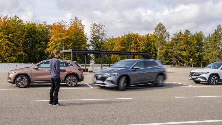 
			Eine Person steht neben einem Parkplatz und beobachtet, wie ein Mercedes-Benz zwischen zwei weiteren Mercedes-Benz-Fahrzeugen einparkt.
		