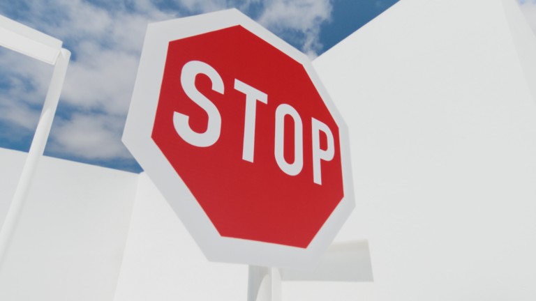 
			Ein rotes Stoppschild vor blauem Himmel mit Wolken und hellem Geb�ude im Hintergrund.
		