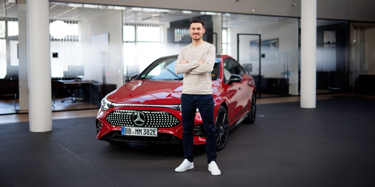 
				Felix B�llmann, Customer Onboarding f�r Digitale Extras bei Mercedes-Benz, steht l�chelnd und mit verschr�nkten Armen vor einem roten, elektrischen Mercedes-Benz CLA.
				