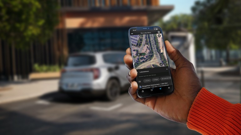 
			Im Vordergrund h�lt eine Hand ein Smartphone, auf dem eine Kartenansicht der Umgebung zu sehen ist, auf dem die Navigation mit Electric Intelligence m�gliche Ladestationen anzeigt. Im Hintergrund ist unscharf ein Mercedes-Benz Fahrzeug an einer Lades�ule zu sehen.
		