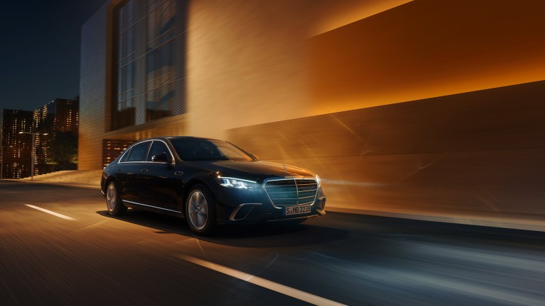 
			Eine neue S-Klasse Limousine von Mercedes-Benz f�hrt mit beleuchteten Scheinwerfern durch eine abendliche, urbane Umgebung.
		