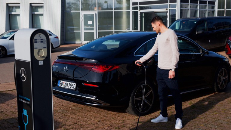 
			Felix B�llmann, Customer Onboarding f�r Digitale Extras bei Mercedes-Benz, steht vor einem Geb�ude neben einer Lades�ule und steckt das Ladekabel in die Buchse eines schwarzen elektrischen Mercedes-Benz CLA.
		