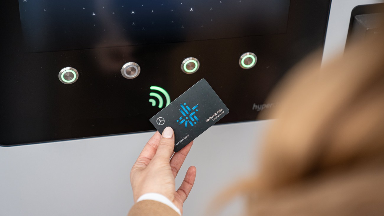 
			Eine Hand h�lt eine MB.CHARGE Public Ladekarte vor einer Lades�ule.
		