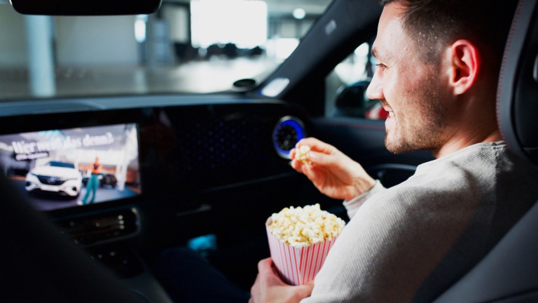 
			Felix B�llmann, Customer Onboarding f�r Digitale Extras bei Mercedes-Benz, sitzt auf dem Beifahrersitz eines Mercedes-Benz CLA und sieht sich auf dem Zentralbildschirm eine Serie an, w�hrend er aus einer Popcornt�te isst.
		