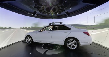 
					  Ein wei�er Mercedes-Benz steht im Handling-Simulator im Mercedes-Benz Technology Center Sindelfingen. Um das Fahrzeug herum ist eine 360-Grad-Leinwand zu sehen, auf der eine Fahrbahn simuliert wird.
					  